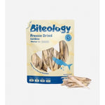 Load image into Gallery viewer, Biteology Freeze Dried Sardine dog treats in a beige stand-up pouch with a blue logo and a clear window showing the freeze-dried fish pieces, with several loose treats placed in front on a light gray background.
